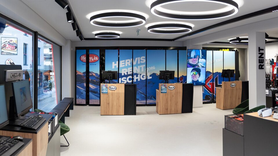 A modern shop with computer workstations and a large window front. The walls are decorated with pictures of mountain landscapes.