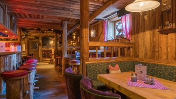 A cozy cabin with wooden interior and warm lighting. There are tables and colorful seating that look inviting.