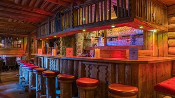 A cozy wooden bar with colorful lights and round stools. The atmosphere is warm and inviting.
