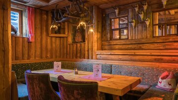 A rustic wood interior with a large table and comfortable seating. The walls are decorated with antlers, and the lighting creates a cozy atmosphere.
