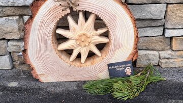 A wooden sign with a carved star and a natural wood surface. Next to it are fresh pine branches and a small card.