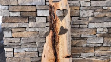 An artistic wooden object with heart shapes and a rustic look. It stands in front of a stone wall and conveys a cozy atmosphere.