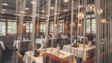A cozy restaurant with elegant tables and atmospheric lighting. The large windows offer a view outside and create an inviting atmosphere.