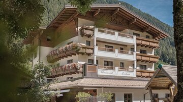 A charming mountain hotel with several balconies and wooden embellishments. Surrounded by a picturesque natural setting.