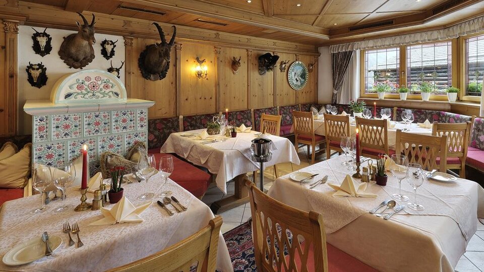 A cozy restaurant with wooden walls and elegant tablecloths. The tables are festively arranged, and the decoration includes traditional hunting trophies.