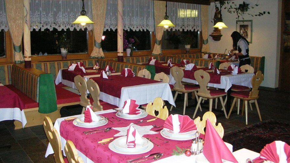 An inviting restaurant with elegant tables covered with red tablecloths and decorative napkins. In the background, a staff member can be seen preparing the service.