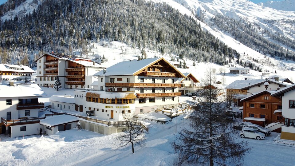 A picturesque winter landscape with snow-covered houses and mountains in the background. The scene radiates tranquility and coziness.