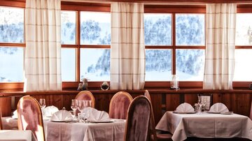 A cozy restaurant with elegant tables and chairs. Large windows offer a view of a snowy landscape.