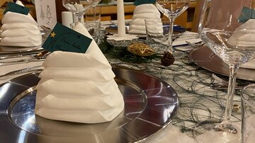 A festively set table with elegantly folded napkins in the shape of a mountain. Glasses and silver cutlery complete the festive atmosphere.