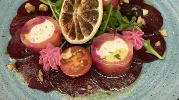 An artistically arranged plate with beetroot, fresh arugula, and stuffed rolls. The dish is decorated with dried lemon and colorful garnishes.