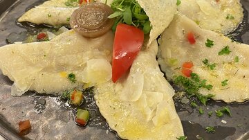 A delicious plate of stuffed dumplings, garnished with cream cheese and fresh vegetables. The dish is placed on a dark plate and is attractively arranged.