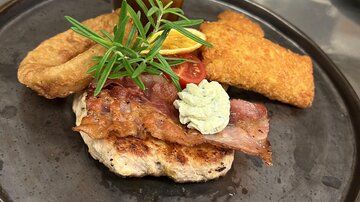 A delicious dish with fried meat, a side dish, and a sauce. Fresh herbs and a slice of lemon garnish the presentation.