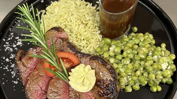 A dish with juicy steak, combined with green rice and peas. Served with a sauce in a jar and fresh herbs.