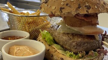A juicy burger made from whole grain bread with lettuce, bacon, and a slice of pineapple. It comes with fries and two different dips.