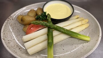 A plate with white asparagus, green asparagus, and small potatoes. There is also a bowl of sauce.