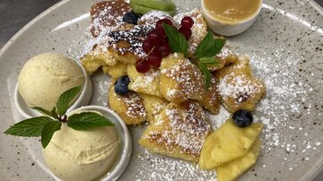 A plate of delicious doughnuts, garnished with fresh berries and mint. It comes with two scoops of ice cream and a bowl of caramel sauce.