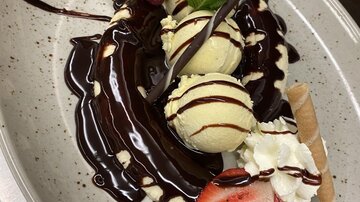 A delicious dessert with vanilla ice cream, chocolate sauce, fresh strawberries, and whipped cream. Garnished with mint and a waffle cone.