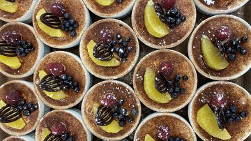 An arrangement of dessert bowls with a golden-brown surface. The desserts are garnished with fruits such as raspberries, blueberries, and lemon slices.