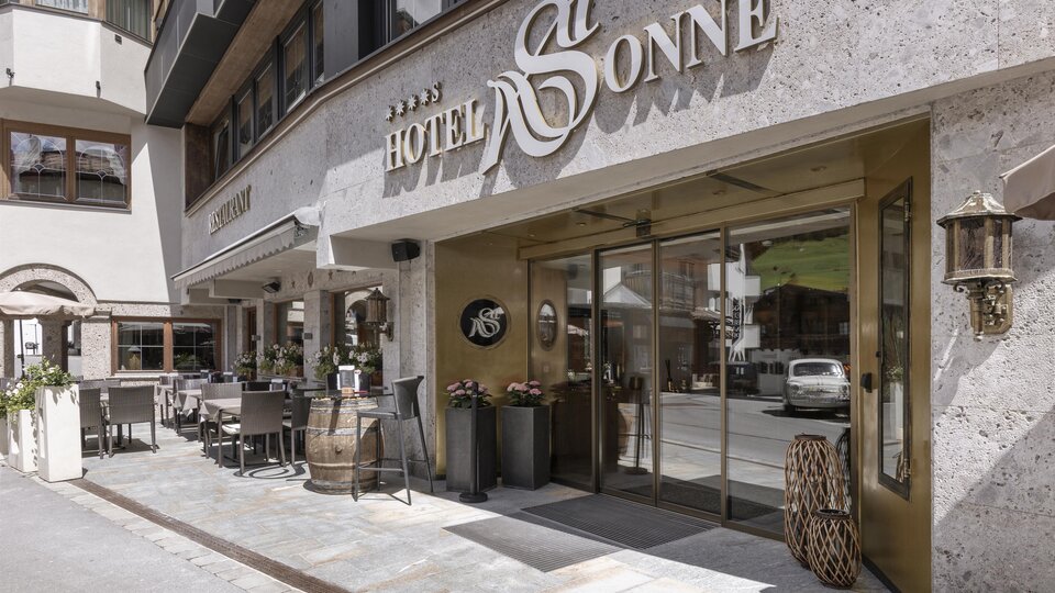 The entrance to the Hotel Sonne is stylishly designed and inviting. There are outdoor seating areas and a modern facade.