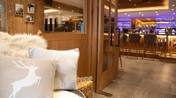 A stylish interior design with wooden paneling and a cozy seating area. In the background, there is an appealing bar with soft lighting.