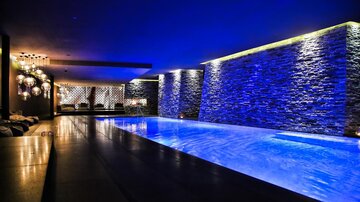 An elegant indoor pool in a dimly lit room, illuminated by blue lights. The walls are designed with modern stone elements, creating a relaxing atmosphere.