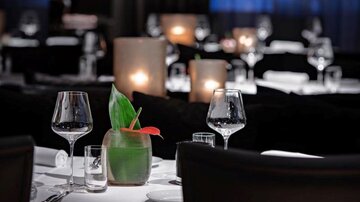 An elegant restaurant with dressed tables and soft lighting. On the table is a decorative plant with a cocktail glass.