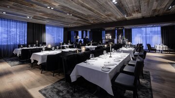 An elegant restaurant with stylishly laid tables and a modern ambiance. The lighting and windows create a cozy atmosphere.