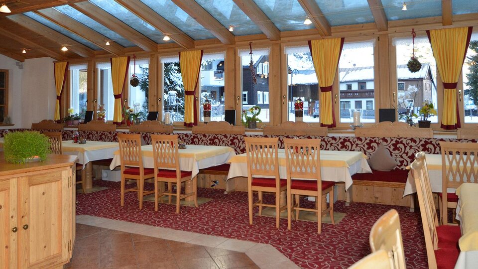 A cozy restaurant area with wooden chairs and tables. Large windows let in plenty of light and offer a view outside.