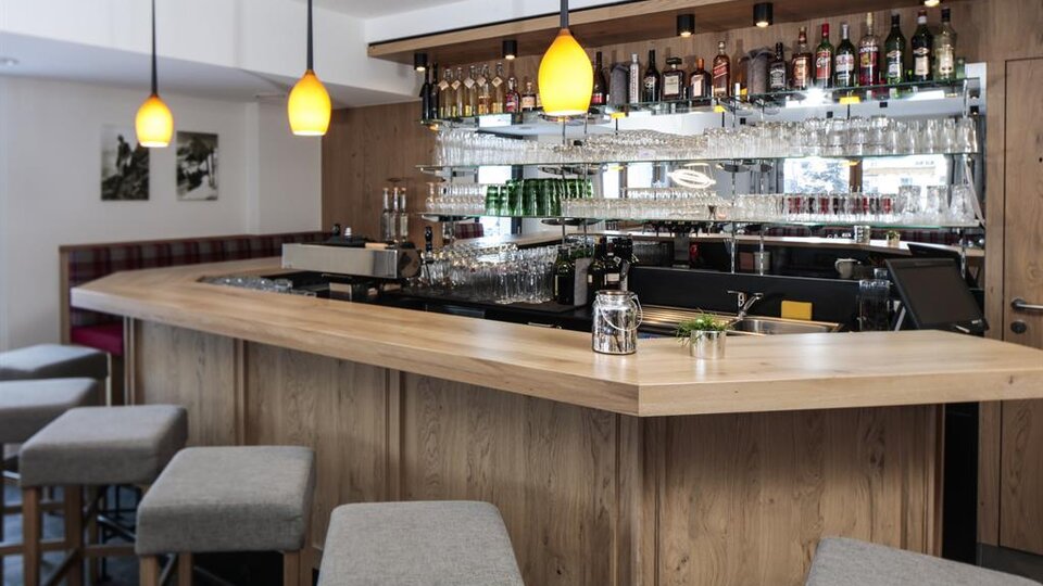 A modern bar with a curved wooden counter and stylish stools. In the background, shelves with a selection of spirits and glasses can be seen.