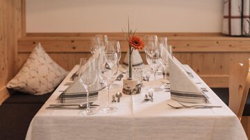 An elegantly set table with glasses and decorated napkins. In the center stands a flower in a vase.