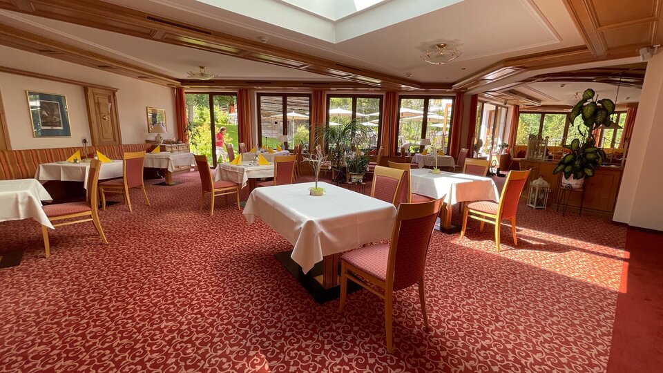 An inviting restaurant with elegant tables and red carpet flooring. Large windows provide plenty of natural light and a pleasant atmosphere.