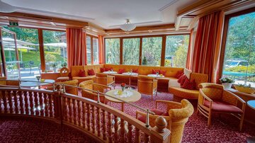 A cozy lounge with comfortable seating and large windows. The warm color scheme and the view of the outdoors create an inviting atmosphere.