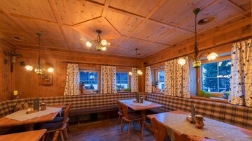 Ein gemütliches Restaurant mit Holzdekor und warmem Licht. Die Tische sind ordentlich gedeckt und die Fenstervorhänge verleihen eine einladende Atmosphäre.