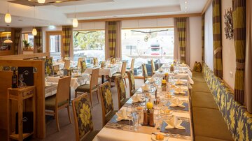 Ein elegantes Restaurant mit festlich gedeckten Tischen. Helle Farben und große Fenster sorgen für eine einladende Atmosphäre.