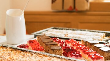 Eine Auswahl an köstlichen Kuchen und Torten auf einem Tisch. Im Hintergrund steht eine kleine Kanne.