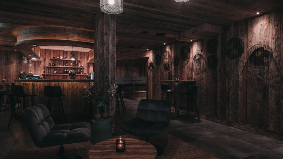 A cozy room with wooden walls and soft lighting. The bar in the background and the modern furniture create an inviting atmosphere.