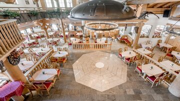 An inviting restaurant with wood-paneled walls and tables in red and white. Large windows provide plenty of daylight and a cozy atmosphere.