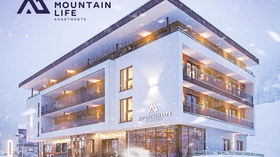 A modern apartment building in the snow, surrounded by a winter landscape. The facade is in light tones and features large windows.