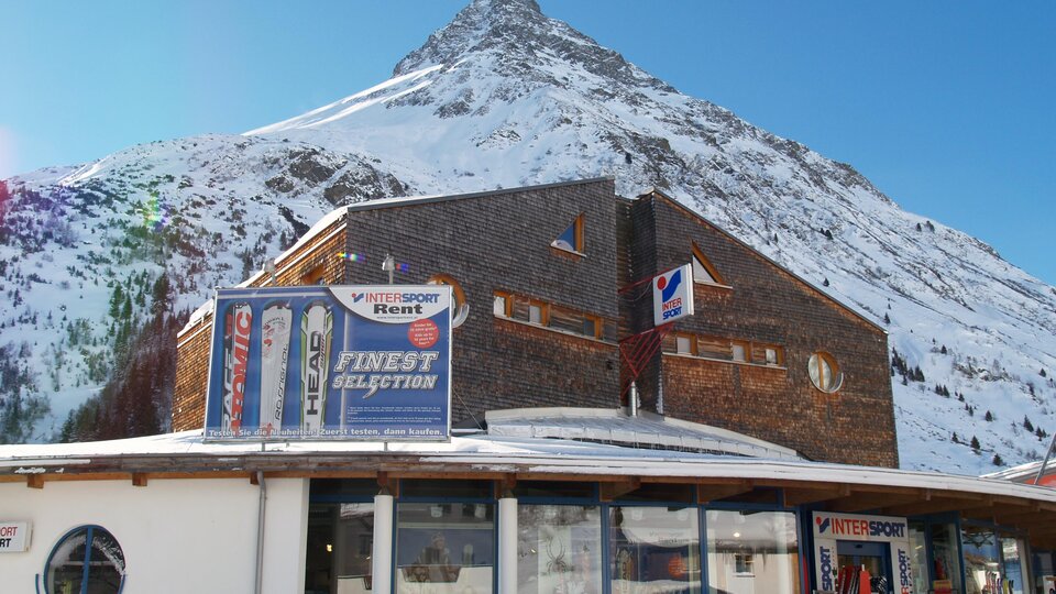A modern building in front of a snow-covered mountain. The clear sky and winter landscape create a picturesque view.