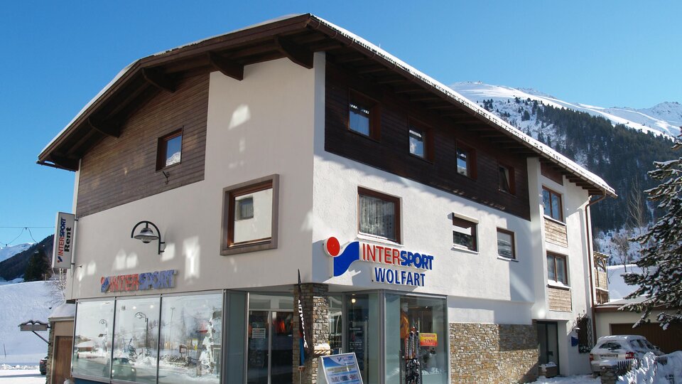Ein sportliches Geschäft in einem schneebedeckten Gebiet. Die Fassade zeigt große Fenster und eine klare Beschilderung.
