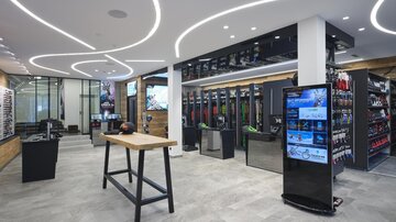 A modern sales room with a bright, minimalist design. Products are neatly displayed on shelves and on a table.