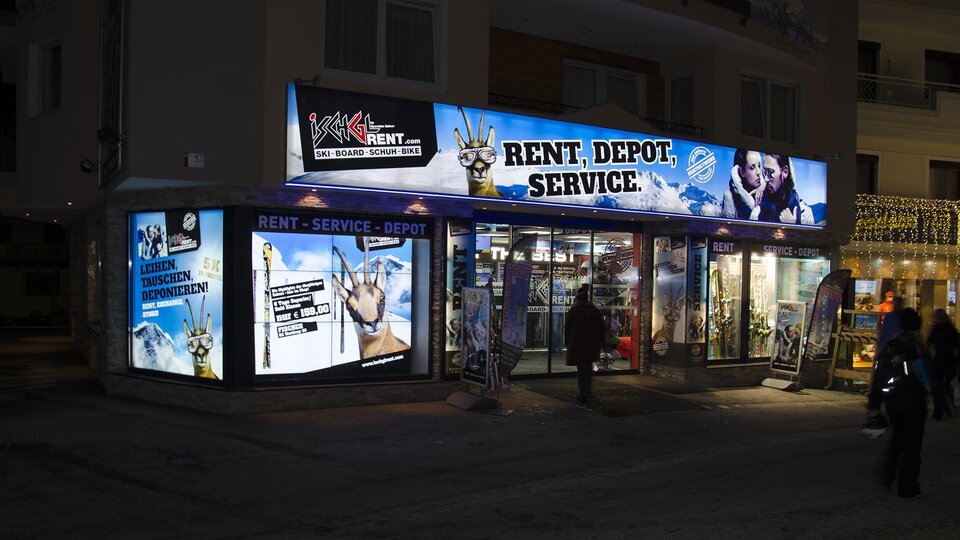 A business with a illuminated facade that offers services such as rental and storage. The advertising is eye-catching and informs about the services offered.