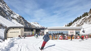 A modern ski hut in a snowy mountain landscape. Skiers are enjoying the sun and the clear weather.