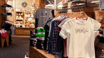 A small store with colorful T-shirts and other clothing items on clothing racks. In the background, additional products and decorations are visible.