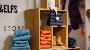 A stylish presentation of children's clothing in a store. Wooden shelves display colorful sweaters, boots, and accessories, surrounded by a fashionable background.