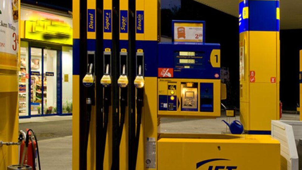 A gas station with several fueling pumps and a cashier area. It is evening, and the surroundings are well-lit.