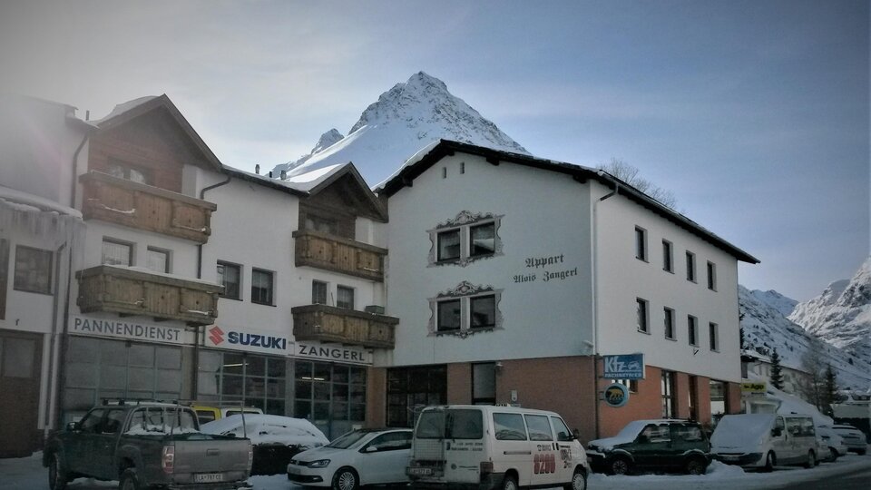 Ein charmantes Gebäude in den Bergen, umgeben von Schnee. Im Hintergrund ist ein majestätischer Gipfel zu sehen.