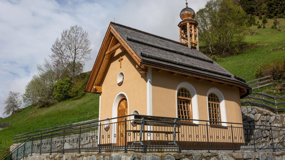 A small chapel on a gentle hill surrounded by trees. The sky is partly cloudy, and the architecture is simple and charming. | © Bernhard Gruber – Photography