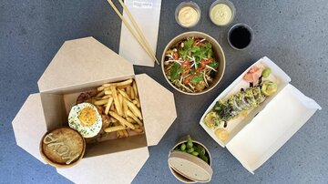 An appetizing selection of food on a table. There are fries, sushi, a salad, and various dips in bowls.