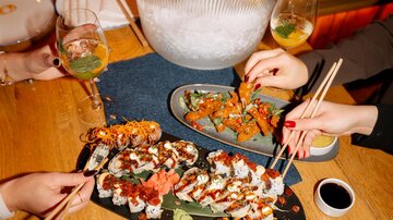 A table with sushi plates and glasses with drinks. In the background, there is an icebox with champagne.